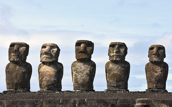 La photo représente cinq statues de pierre monumentales (appelées Moaï) de l’Île de Pâques.