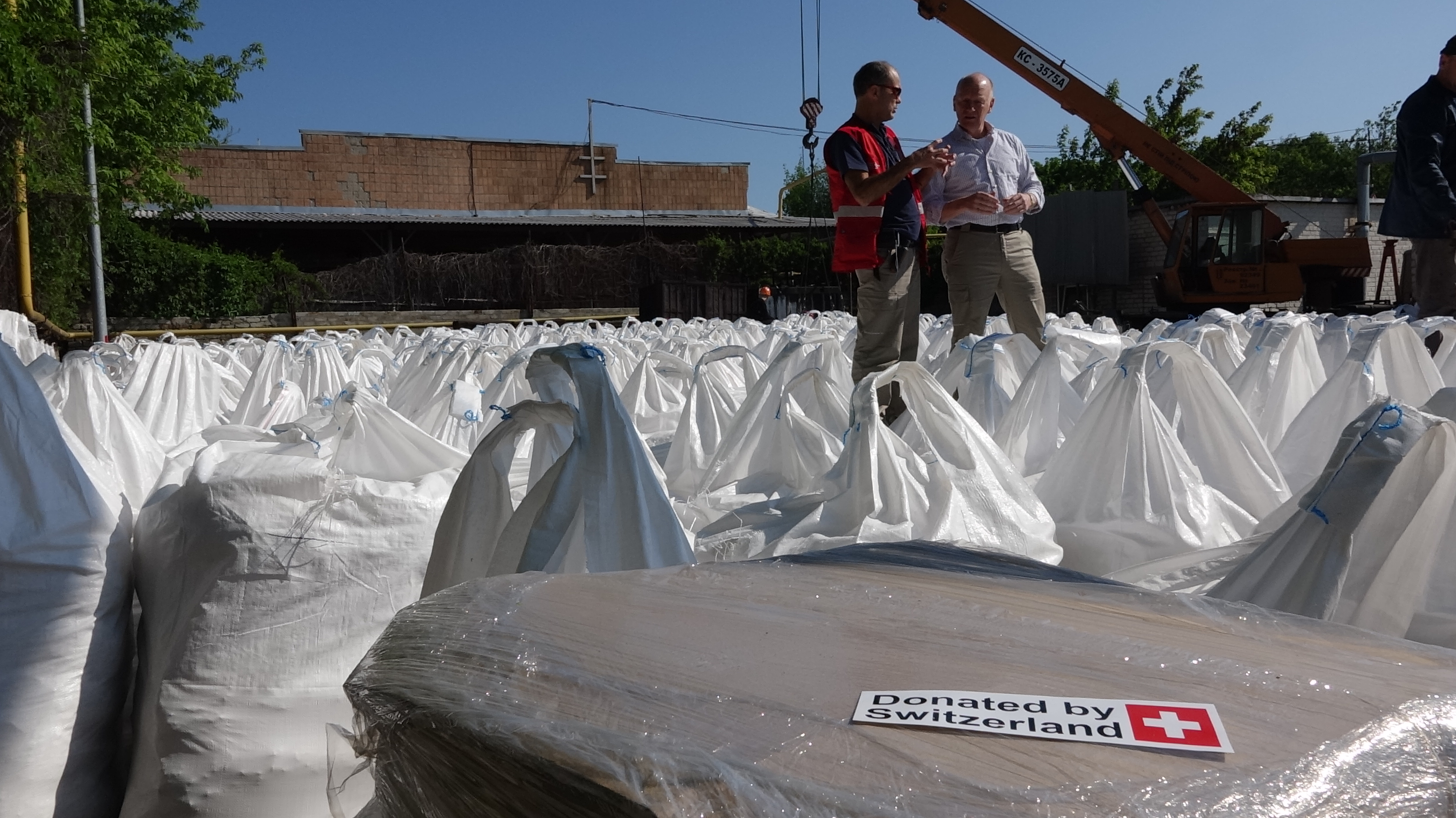 Due esperti svizzeri in mezzo a un centinaio di sacchi di prodotti chimici ammassati a terra nell'area adiacente a una stazione di distribuzione idrica.   