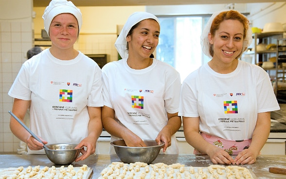 Three young women apprentices filling two baking trays with pastries. 