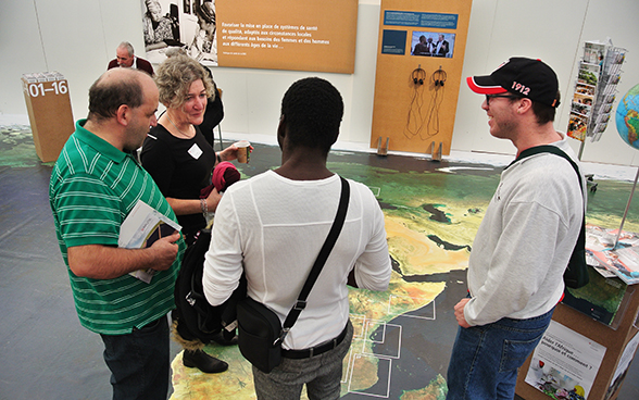 Three visitors listen to a member of SDC staff at the stand. © FDFA