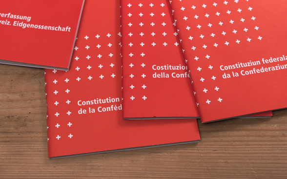 Copie della Costituzione federale svizzera nelle quattro lingue nazionali su una superficie in legno.