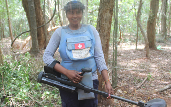 Une femme travaillant pour l'organisation The Halo Trust recherche des mines dans une forêt avec un détecteur de mines.