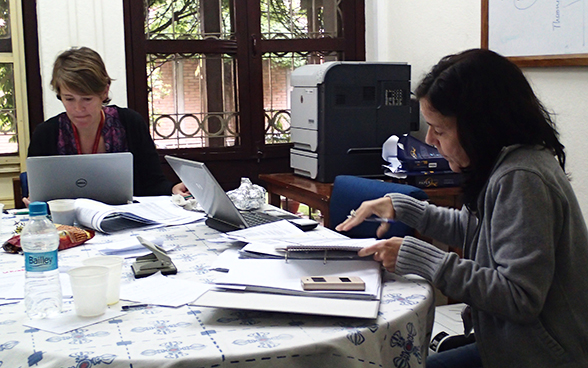 Due collaboratrici dell’Ambasciata di Svizzera in Nepal lavorano sedute a un tavolo con i computer e i documenti.
