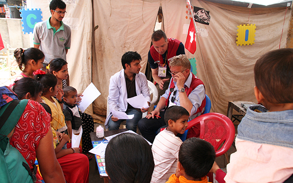 Ein einheimischer Arzt und zwei Schweizer nehmen vor dem Regionalspital Gorkha City Patientinnen und Patienten auf. 