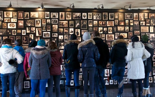 Eine Gruppe von jungen Schweizerinnen und Schweizern betrachtet eine Wand mit Porträts von Opfern des Holocausts. 