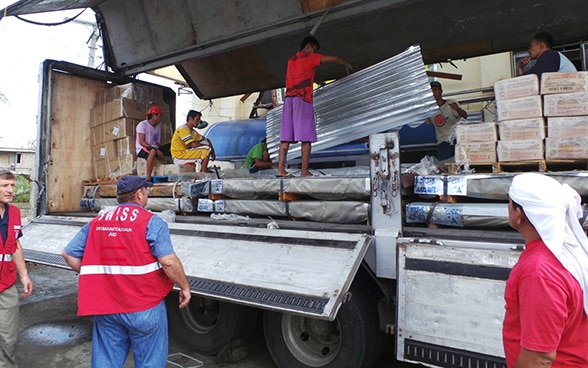 Members of the Swiss Humanitarian Aid Unit and local people from the island of Leyte in the Philippines unload a lorry carrying Swiss Humanitarian Aid relief supplies