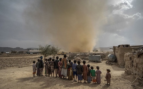 Eine Gruppe afrikanischer Kindern schaut einem Sandsturm in einer dürren sandigen Umgebung zu. 