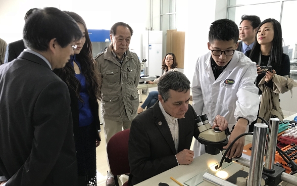 Il consigliere federale Ignazio Cassis seduto davanti a un microscopio insieme a studenti dell’Accademia cinese delle scienze.