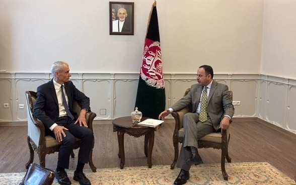 L'ambassadeur Thomas Kolly et le ministre afghan des Finances, H.E. Eklil Hakimi, à une table lors de la signature de l'accord-cadre. Les drapeaux des deux états sont visibles en arrière-plan.