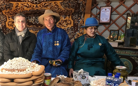 Il consigliere federale Cassis seduto ad una tavola riccamente allestita con due allevatori mongoli.