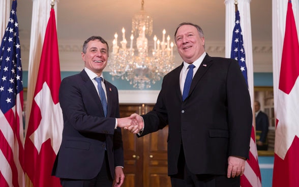 Il consigliere federale Ignazio Cassis stringe la mano al segretario di Stato americano Mike Pompeo a Washington. Sullo sfondo si vedono le bandiere della Svizzera e degli Stati Uniti.