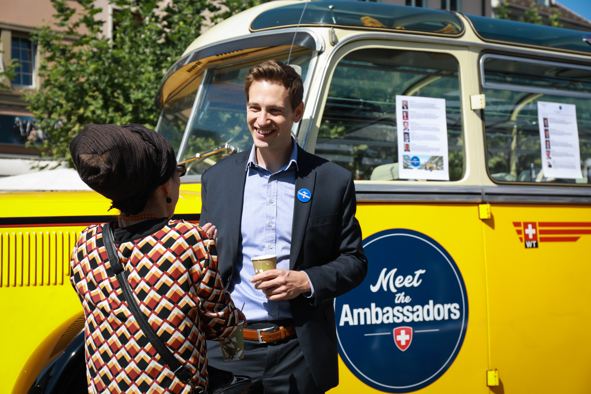 Un ambasciatrice parla con un visitatore; sullo sfondo la corriera postale Meet the Ambassador