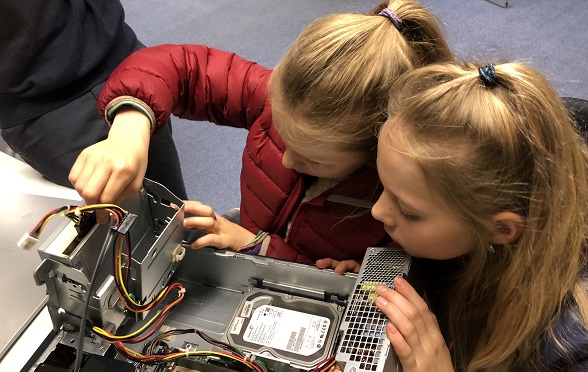 Two girls are handling the inside of a computer.