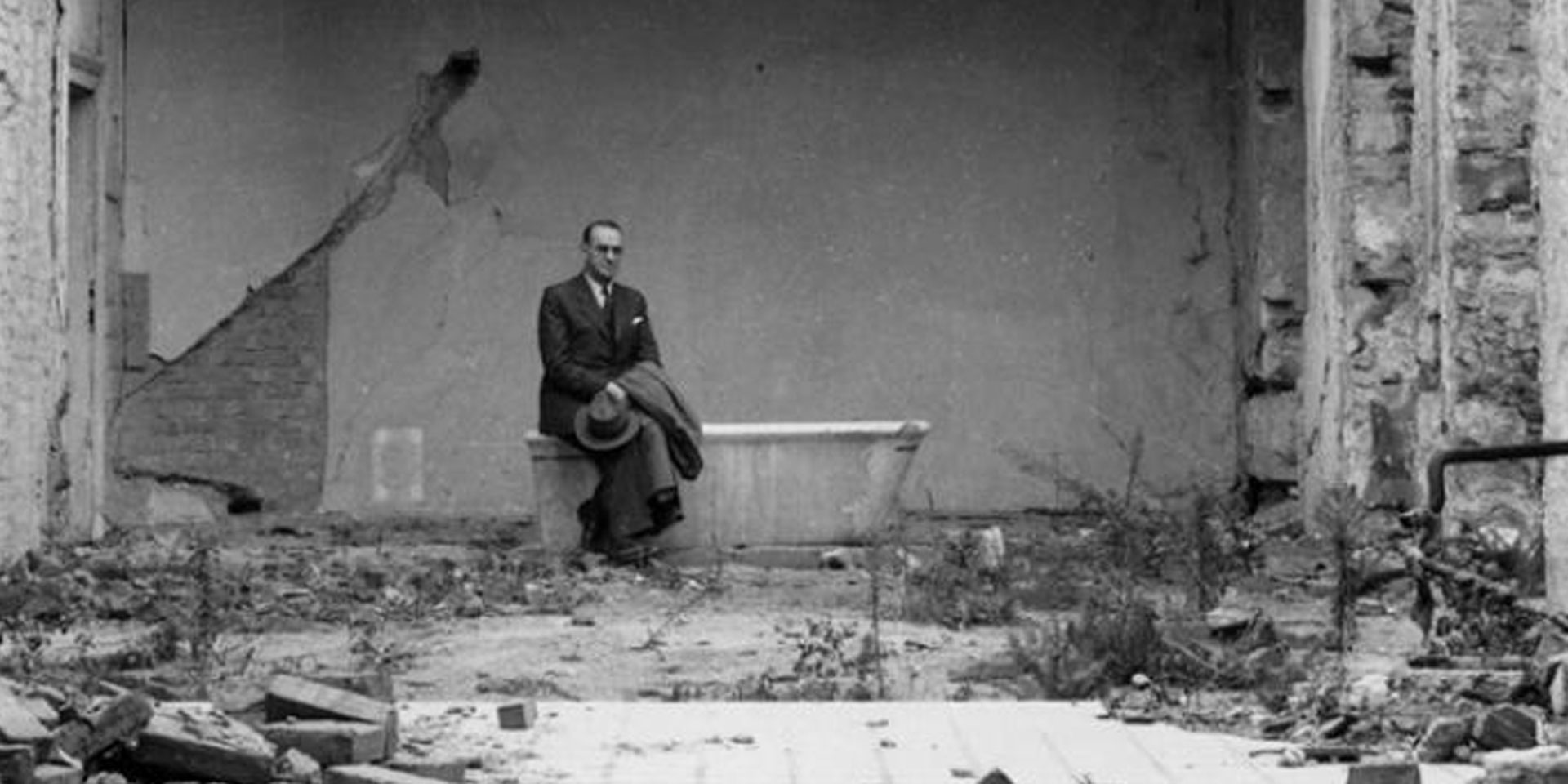 Carl Lutz sitting on a bathtub in a war-ravaged room.