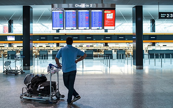 Un homme étudie l'horaire des départs dans la salle d'embarquement d'un aéroport. 