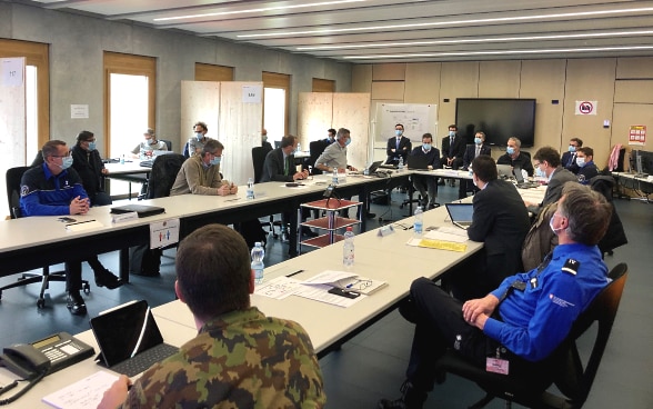 Bundesrat Cassis sitzt an einem langen Sitzungstisch mit Mitgliedern der kantonalen Notfallzentrale und diskutiert mit ihnen.