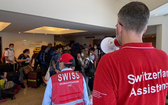 Un collaboratore dell'Ambasciata svizzera dà istruzioni ai viaggiatori con un megafono