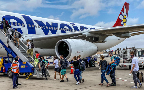 Ein Flugzeug, davor die Flugtreppe, über die eine Reihe von Passagieren einsteigen. 