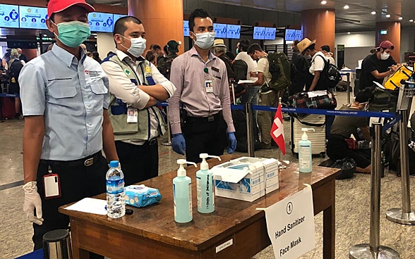 Trois employés de l'ambassade sont debout à une table avec des produits d'hygiène et de désinfection.