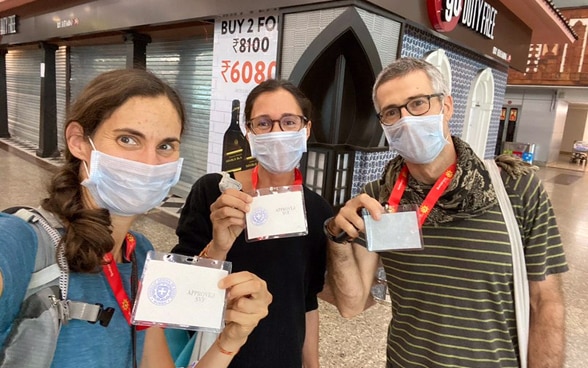 Three passengers wearing masks proudly display their Indian customs clearance badges to board the next flight to Switzerland. 
