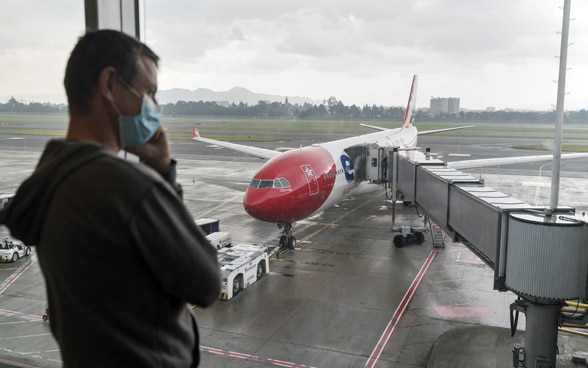 Ein Reisender telefoniert kurz vor dem Abflug der Schweizer Reisenden aus Suedamerika am Dienstag, 24. Maerz 2020, am Flughafen von Bogota, Kolumbien.Die Reisenden wurden wegen der Reise- und Aufenthaltsbeschraenkungen aufgrund des weltweiten Coronavirus-Ausbruchs in einer Sondermaschine (im Hintergrund) in die Schweiz zurueckgeflogen. In der vom Eidgenoessischen Aussendepartement EDA gecharteten Maschine der Fluggesellschaft Swiss sassen 279 Schweizer und 35 Staatsangehoerige aus benachbarten Laendern.