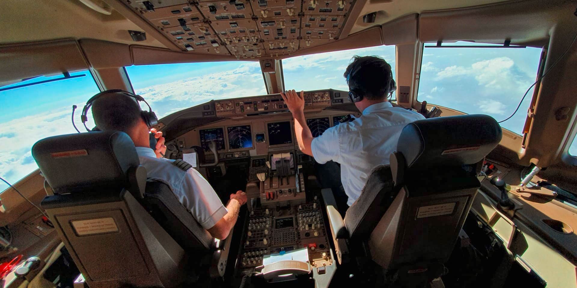 Zwei Piloten im Cockpit eines Flugzeugs. Unter ihnen liegt das Wolkenmeer. 