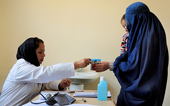 A female doctor gives a woman holding a baby a packet of medicine.