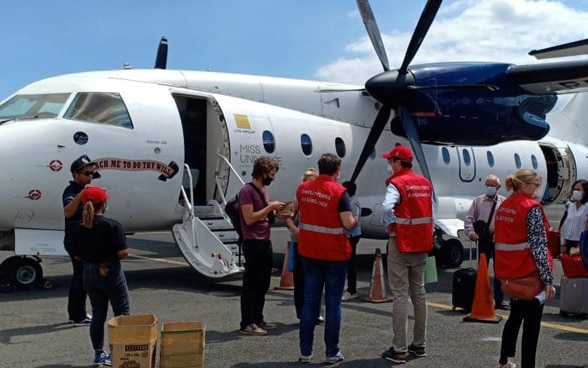  Des passagers et des membres de l'ambassade de Suisse devant devant un avion sur la piste de l’aéroport.