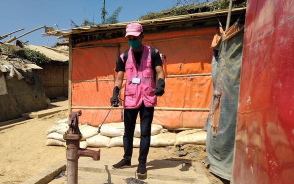 Ein Mann in einer rosaroten Jacke desinfiziert einen Brunnen in einem Flüchtlingslager in Bangladesch.