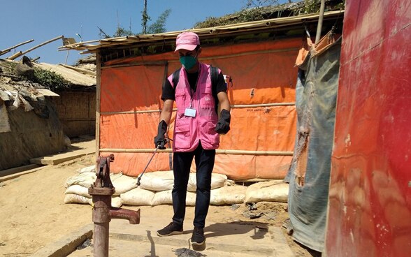 Un uomo con una giacca rosa disinfetta un pozzo in un campo profughi in Bangladesh. 