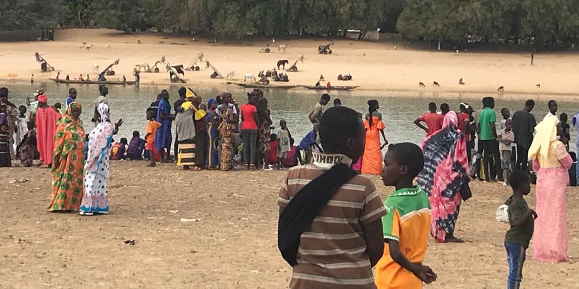 Am Senegalfluss, der Senegal und Mauretanien trennt, stehen bunt gekleidete Menschen am Ufer.