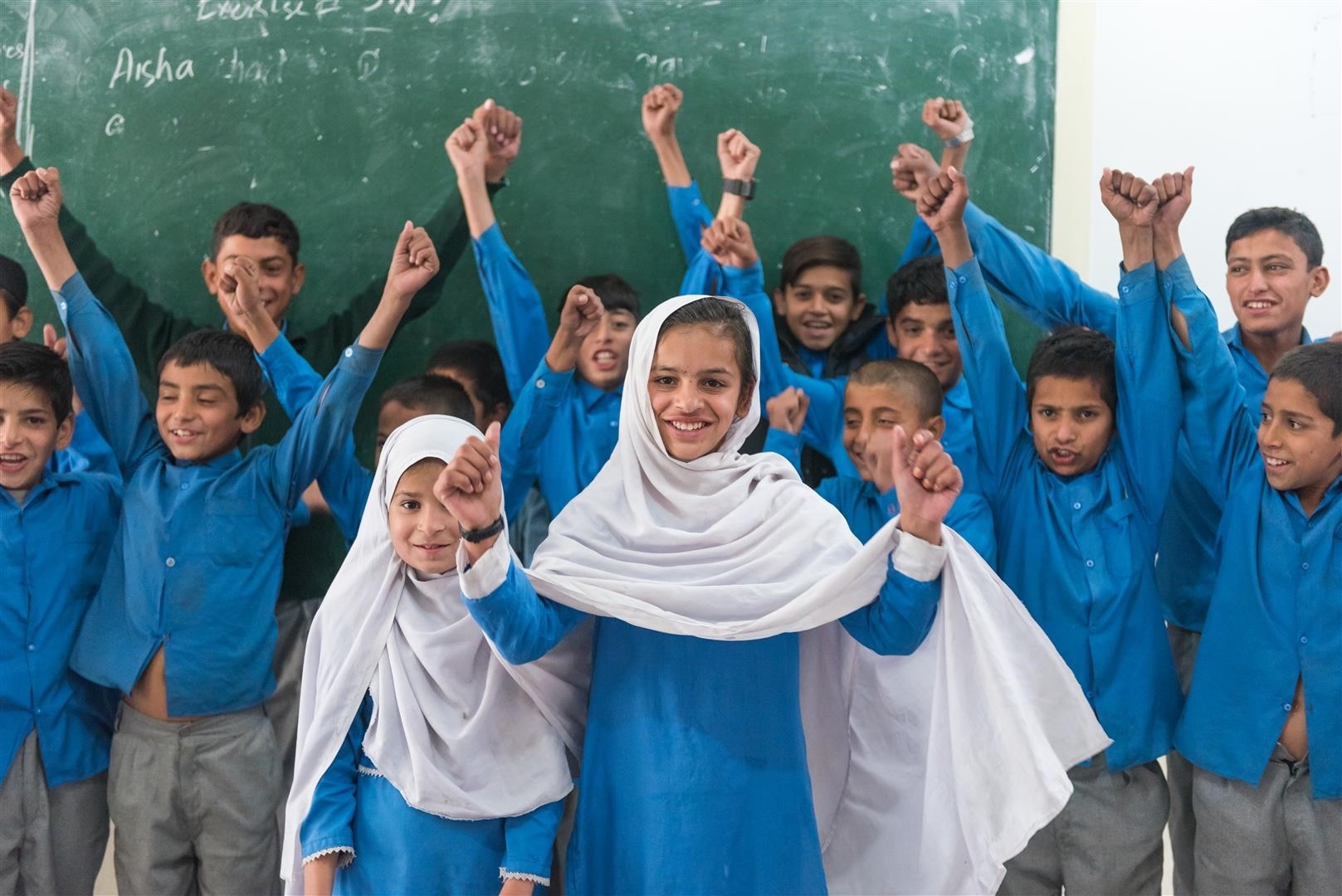 Eine Schulklasse in Pakistan steht vor einer Tafel und hat Freude.
