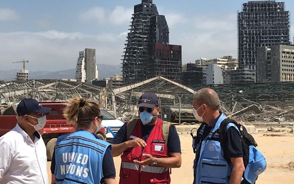 Ein Mitglied der Expertengruppen der Humanitären Hilfe der Schweiz im Gespräch mit Experten der UNO. Im Hintergrund die zerstörte Stadt.