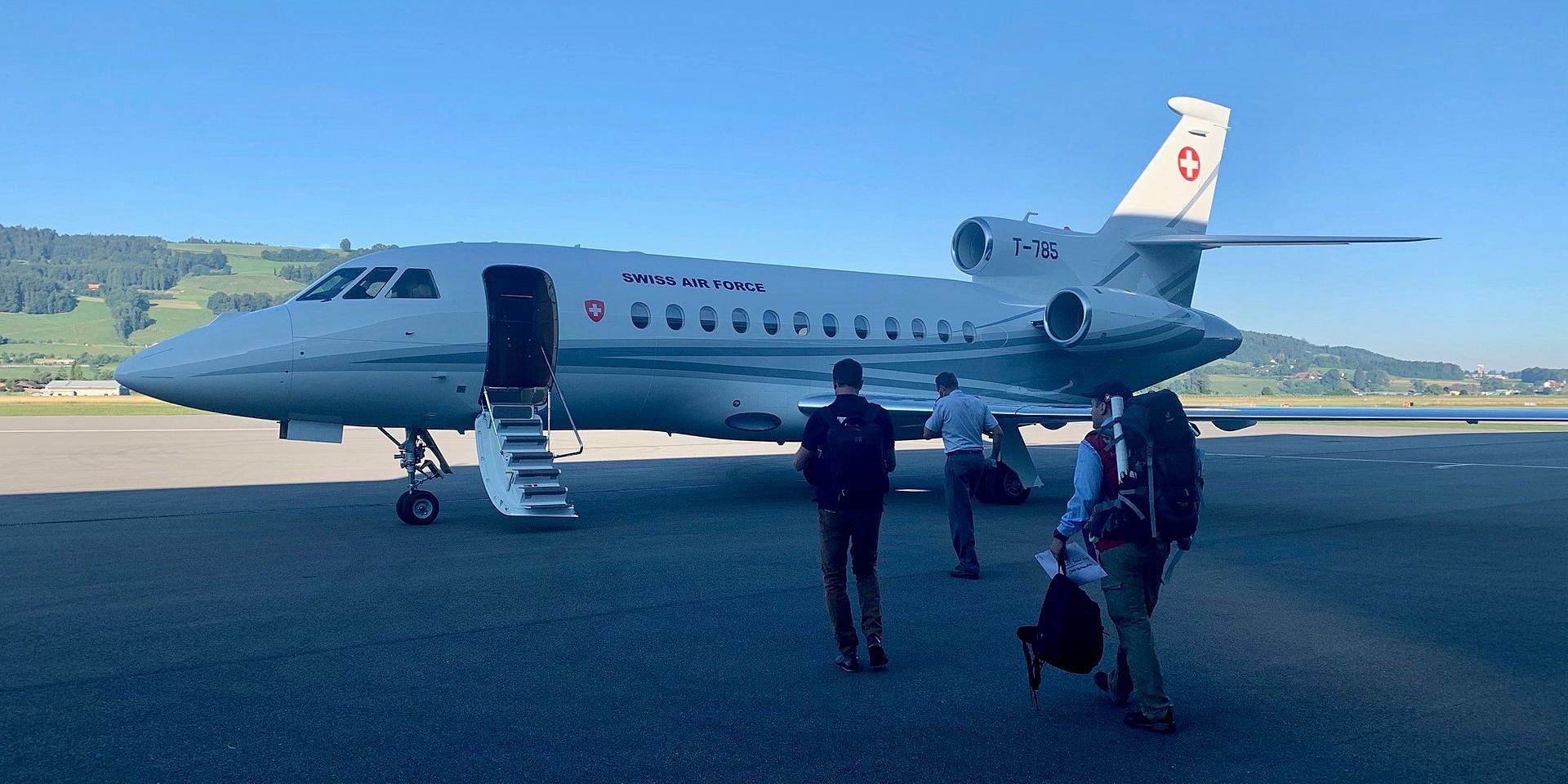 Three people go to a plane that is standing on the tarmac.