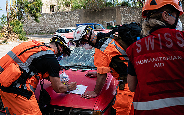 Tre esperti del Corpo svizzero di aiuto umanitario discutono un piano d'azione sul cofano di un veicolo in panne.