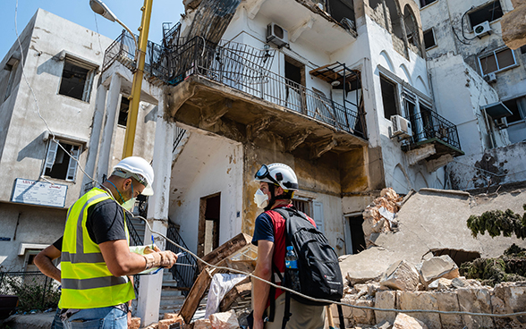 Un esperto del Corpo svizzero di aiuto umanitario è in piedi con un esperto libanese davanti alle macerie di una casa.