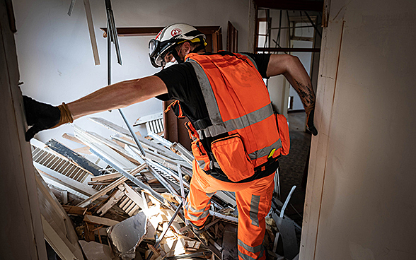 An expert from the Swiss Humanitarian Aid Unit is climbing over debris in a house. 