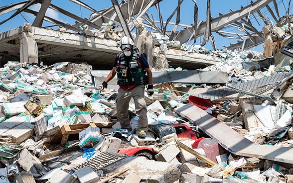 Un expert de l'Aide humanitaire de la Confédération descend d'un tas de décombres. Sur la photo, on peut voir, entre autres, des véhicules et des parties de bâtiments.