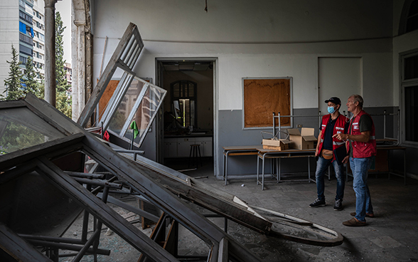 Deux experts du Corps suisse d'aide humanitaire regardent à travers le mur d'une salle de classe.