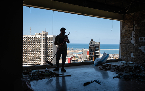 Un cittadino ripulisce un’abitazione distrutta in un condominio con vista sul porto di Beirut.