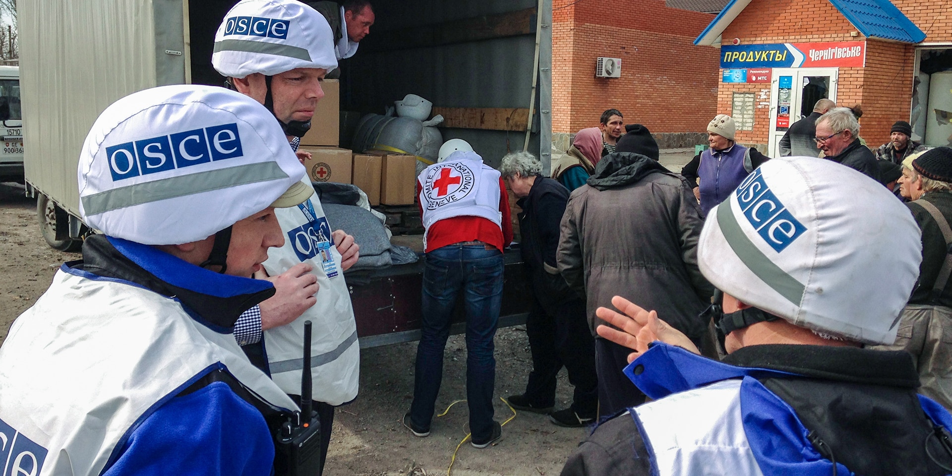 Trois membres de la mission de l'OSCE observent la remise des paquets d'aide à la population ukrainienne.