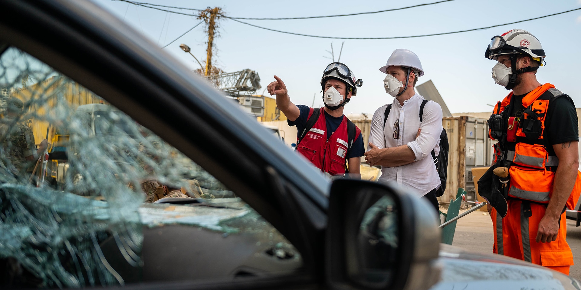 Three experts from the Humanitarian Aid Unit stand by a damaged car.