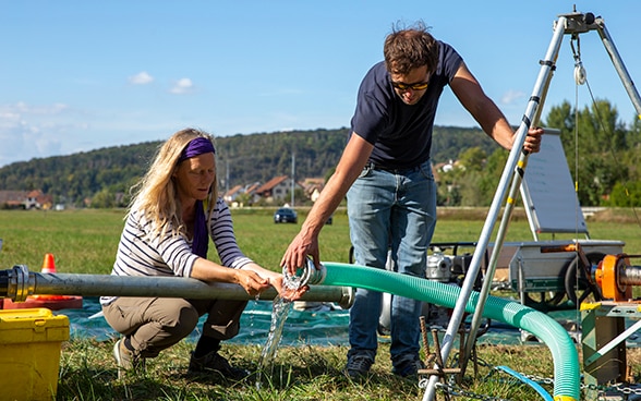 Two experts lift up pipes from which water is running.