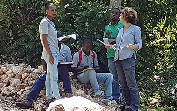 Constance Jaillet, debout et quelques feuilles en main, parle avec quatre autres personnes locales.