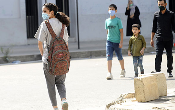 A young girl wears a mask and goes to school with her backpack on.