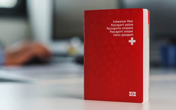 Un passeport suisse est dressé à la verticale sur un bureau blanc.