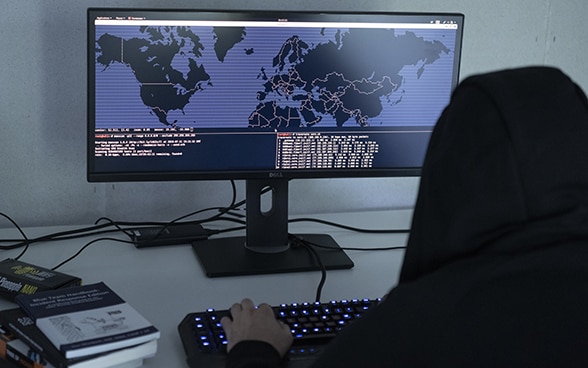 To symbolise cybercrime, a man in a hooded sweatshirt sits in front of a computer displaying a map of the world and modifies programming codes.