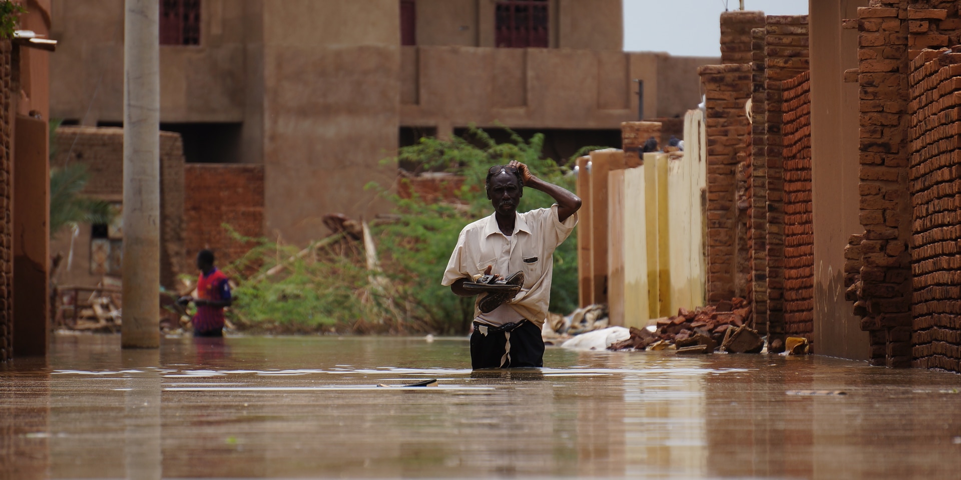 A man walks down a street, his legs completely submerged by water.