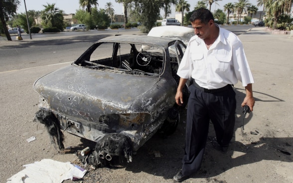 Ein irakischer Polizist inspiziert ein ausgebranntes Auto.