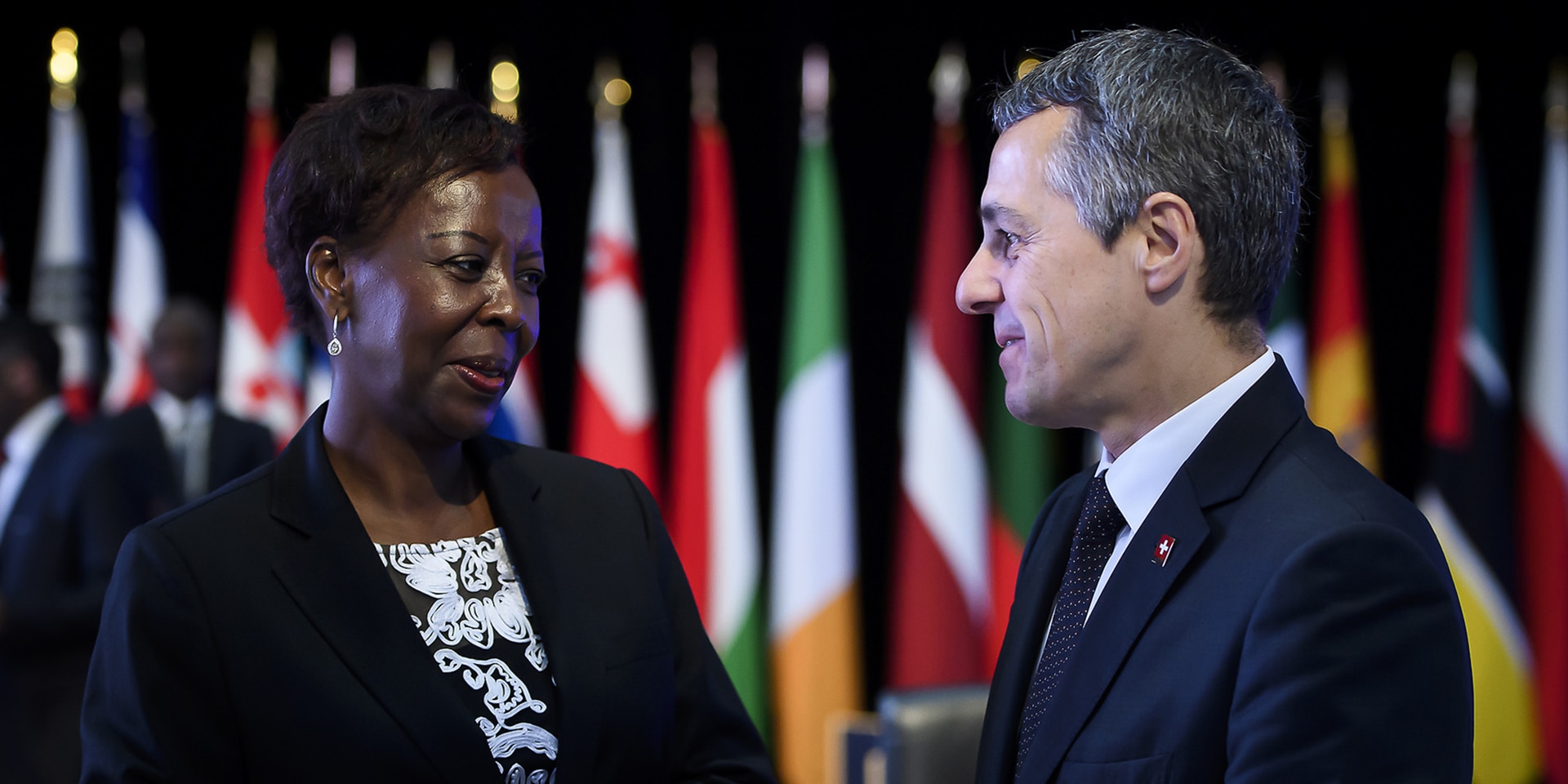 Ignazio Cassis parla con la segretaria generale della Francofonia Louise Mushikiwabo. Sullo sfondo, le bandiere dei 54 Stati membri dell’organizzazione internazionale.